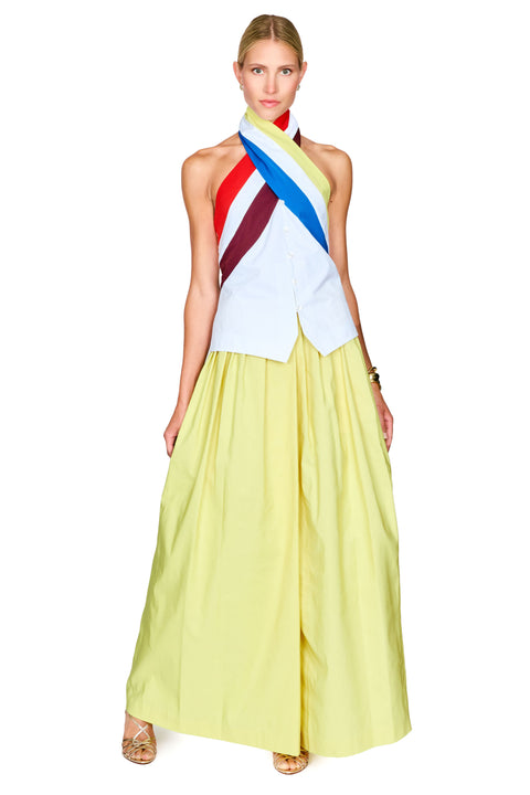 A model wearing a sleeveless halter top with diagonal red, yellow, blue, and white stripes, paired with a flowing pale yellow skirt.