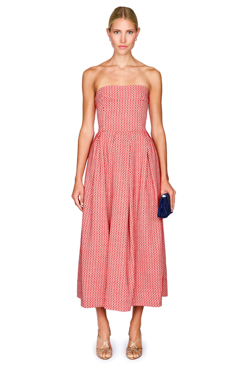 A woman modeling a strapless midi dress with a pink and white geometric pattern, holding a small navy blue clutch against a plain white background.