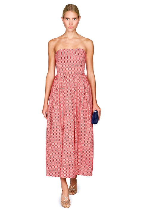 A woman modeling a strapless midi dress with a pink and white geometric pattern, holding a small navy blue clutch against a plain white background.