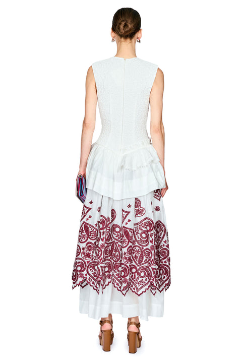 A model shown from the back wearing a sleeveless white dress with a structured corset-style upper back, a ruffled peplum hem, and a long white skirt featuring a burgundy paisley pattern.