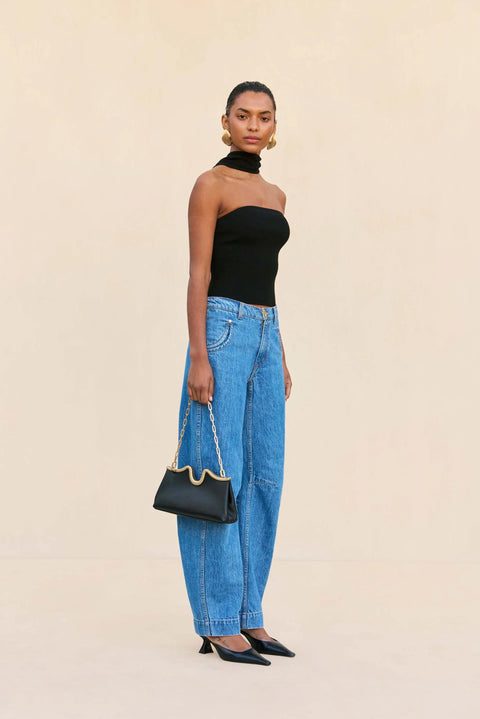 Woman wearing a black strapless top and blue jeans, holding a black handbag on a beige background