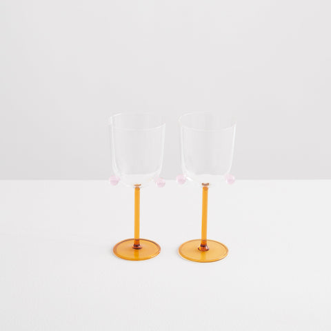 Two Maison Balzac wine glasses with orange stem and pompom detail.